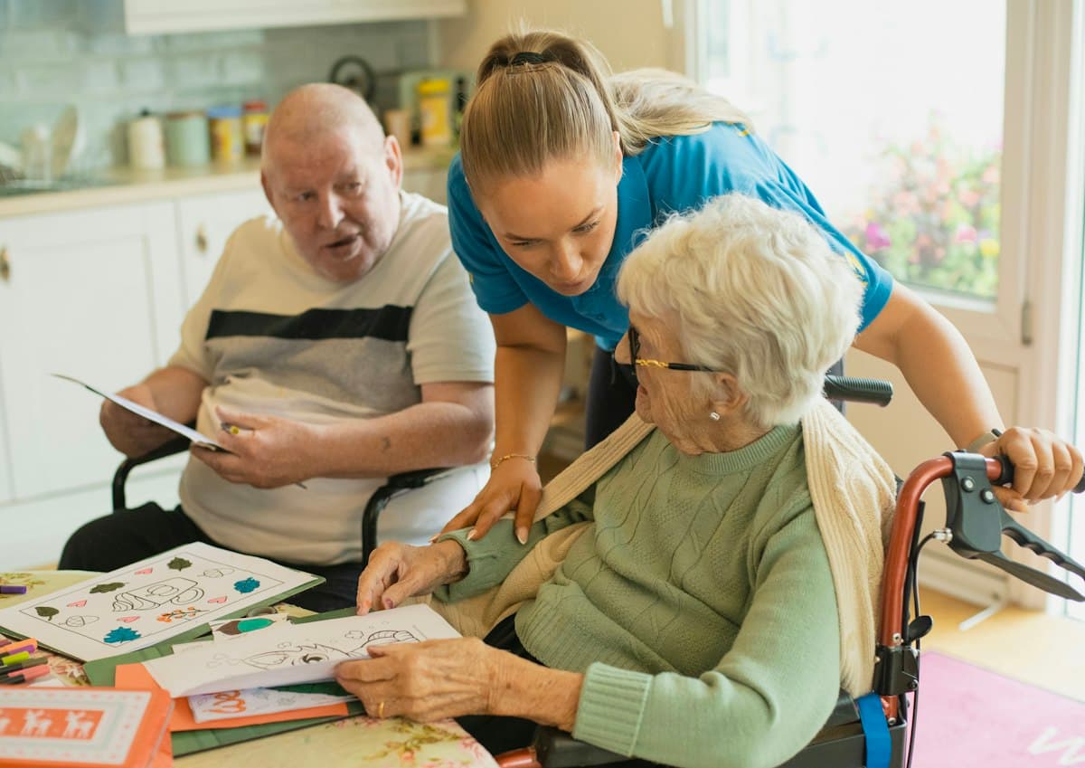 A caregiver leaning in to help an elderly couple with a colouring activity