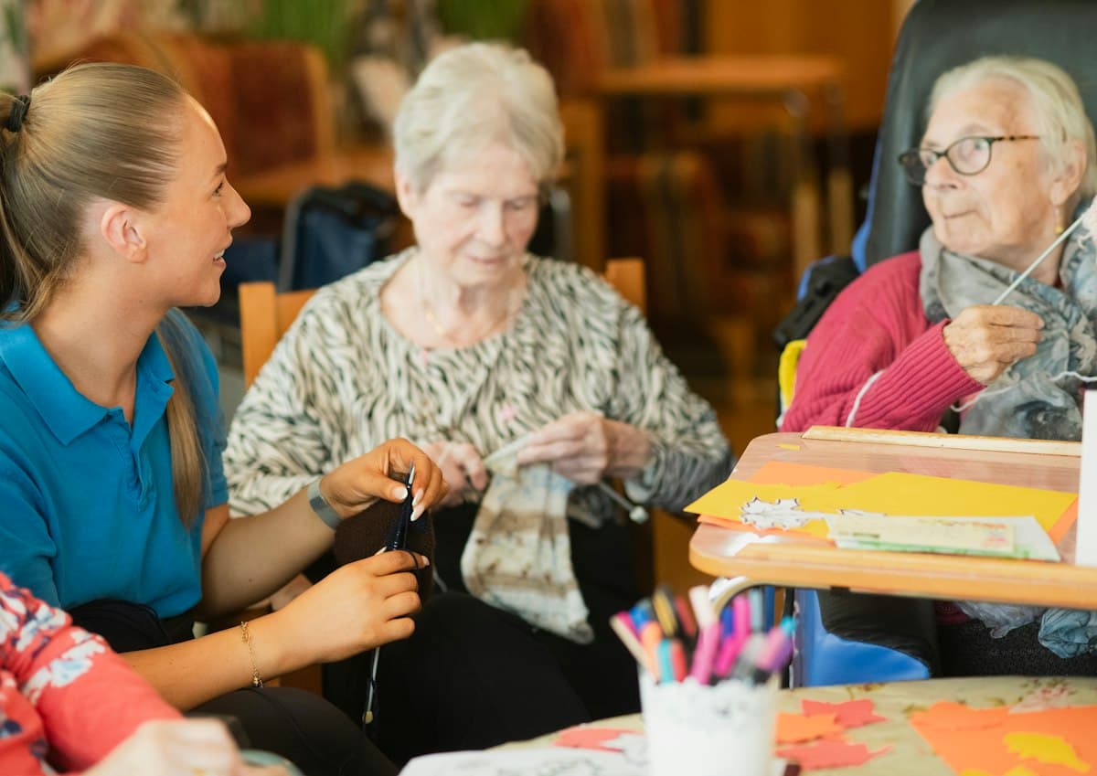 A caregiver knitting with two elderly women at a table