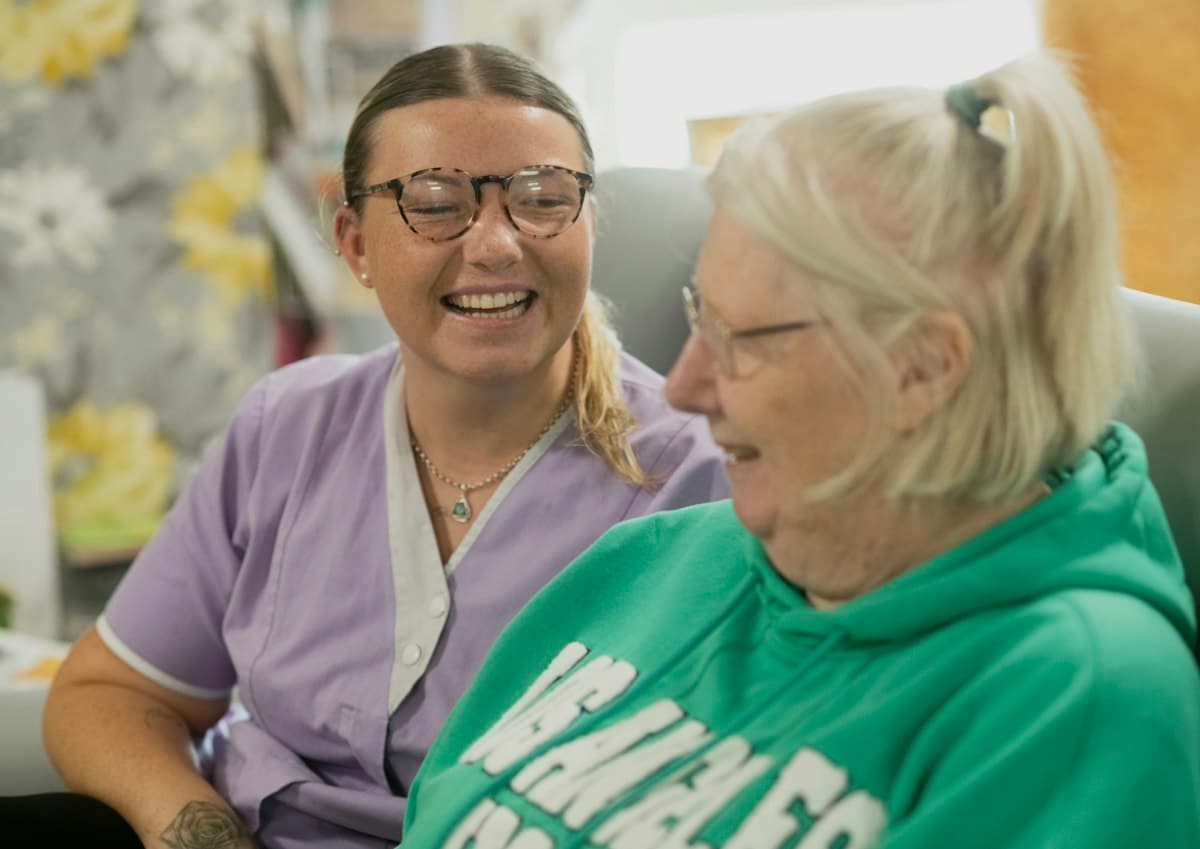 A caregiver and an elderly woman laughing together
